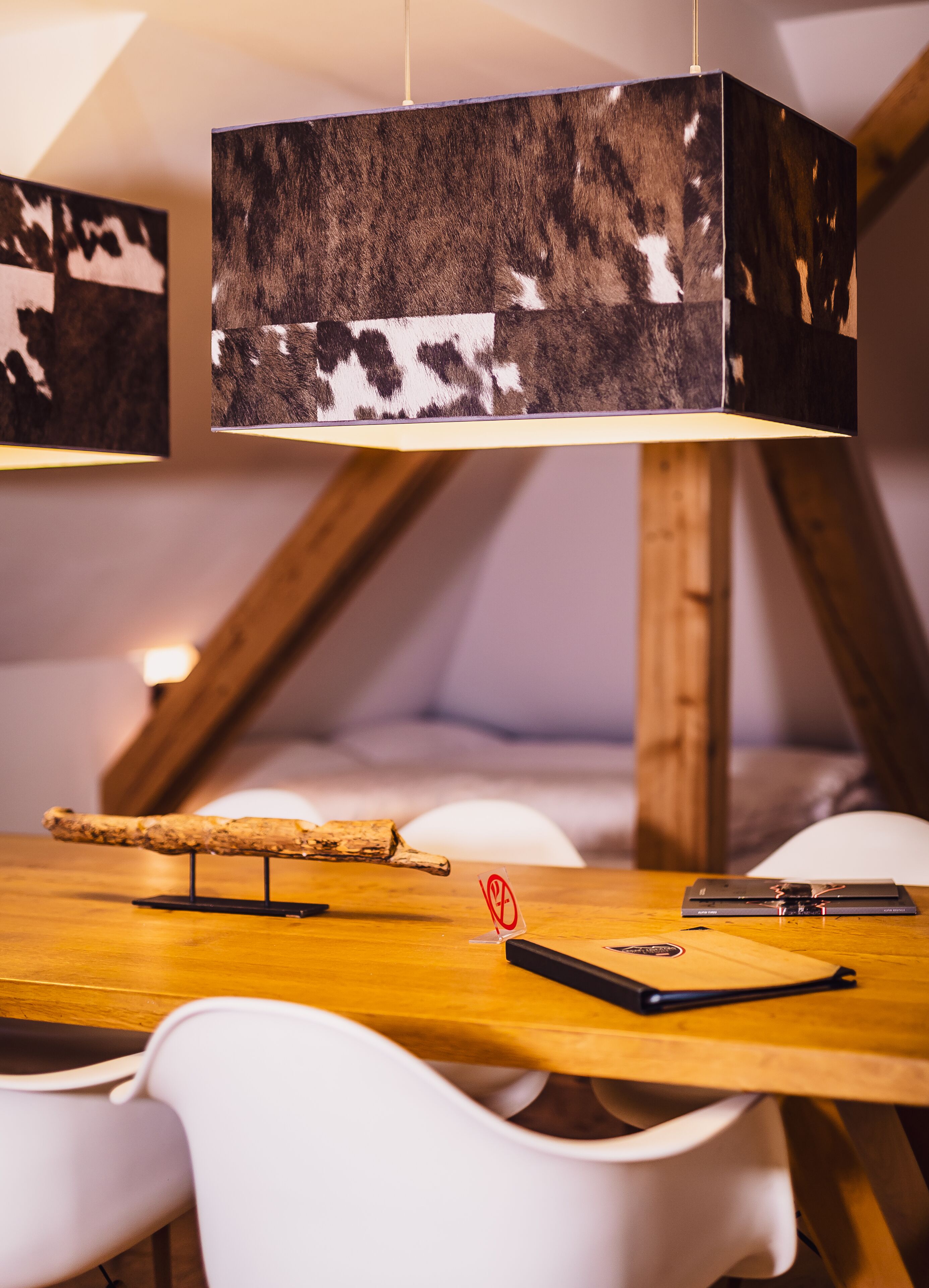 Una mesa de comedor de madera con una lámpara colgante rústica, sillas blancas y una pequeña escultura de madera.