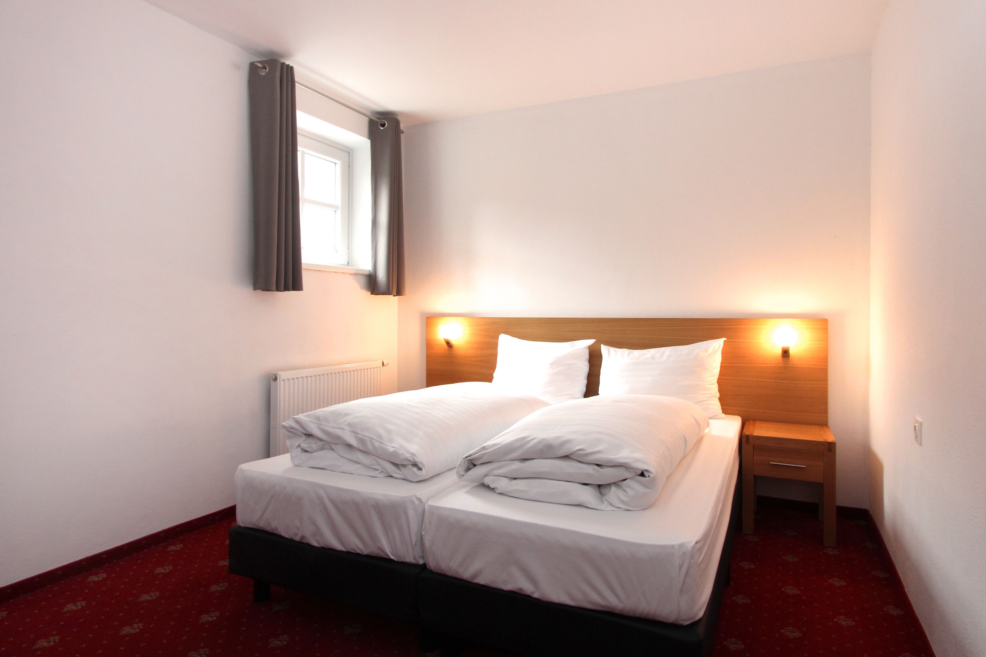 A neatly made double bed with white linens, a wooden headboard, and bedside lamps.