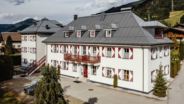 A two-story building with a red balcony, a staircase, and a car parked in front. - Kitz Residenz by Alpin Rentals - incl Summercard (Kaprun)