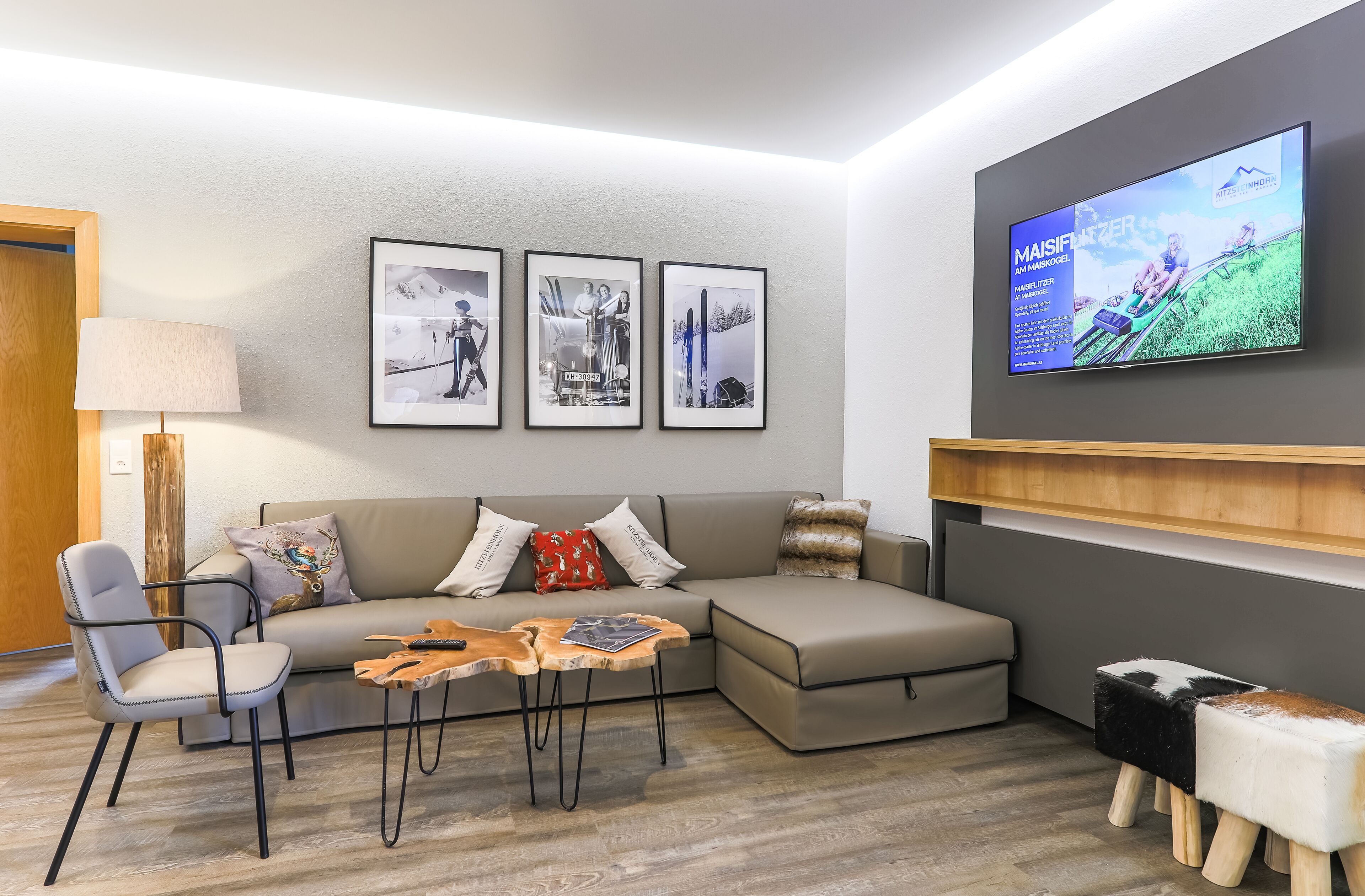 Un salon moderne avec un canapé, un fauteuil, une table basse et un téléviseur fixé au mur qui diffuse une publicité.