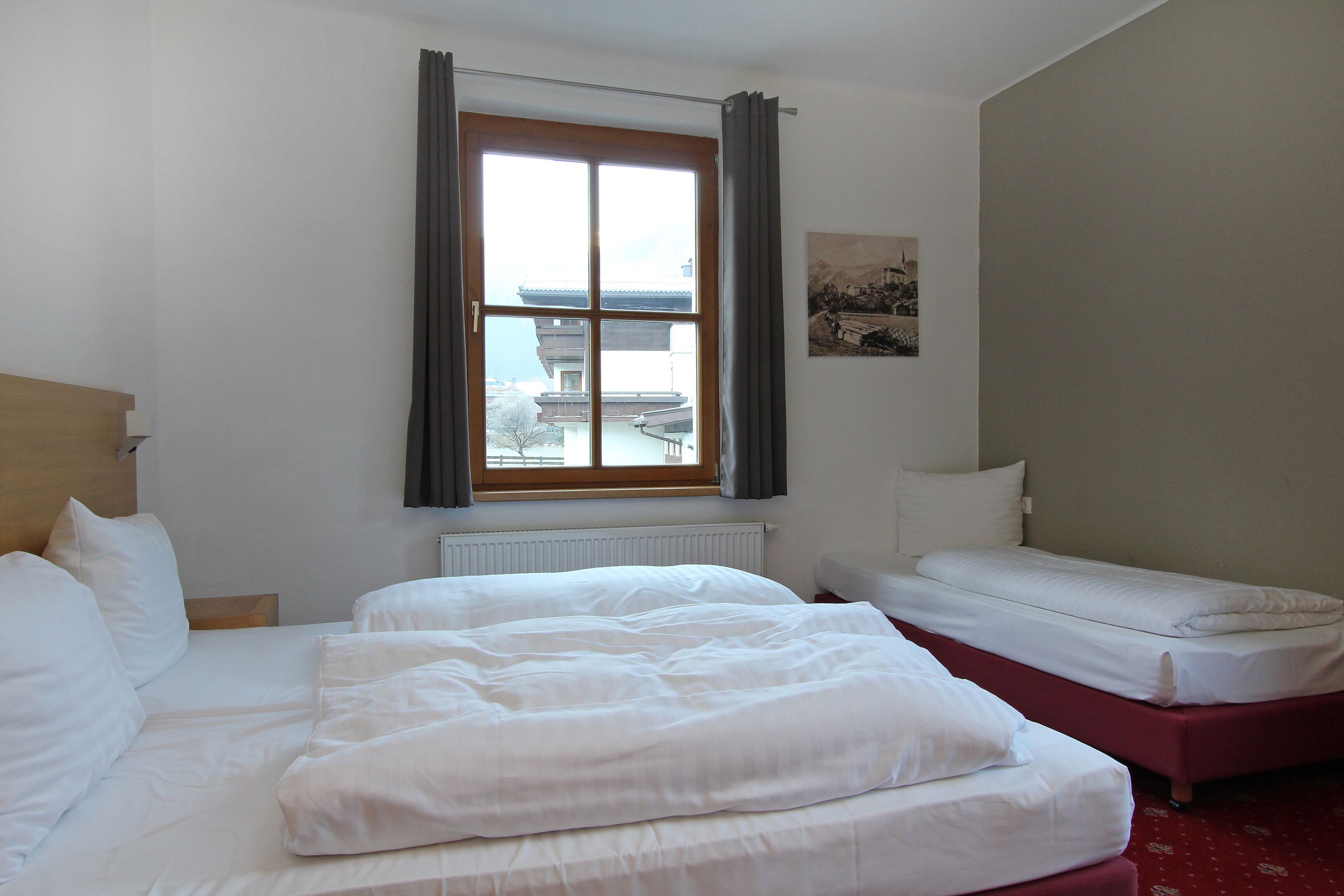 A hotel room with a large bed, a smaller bed, and a window with curtains.