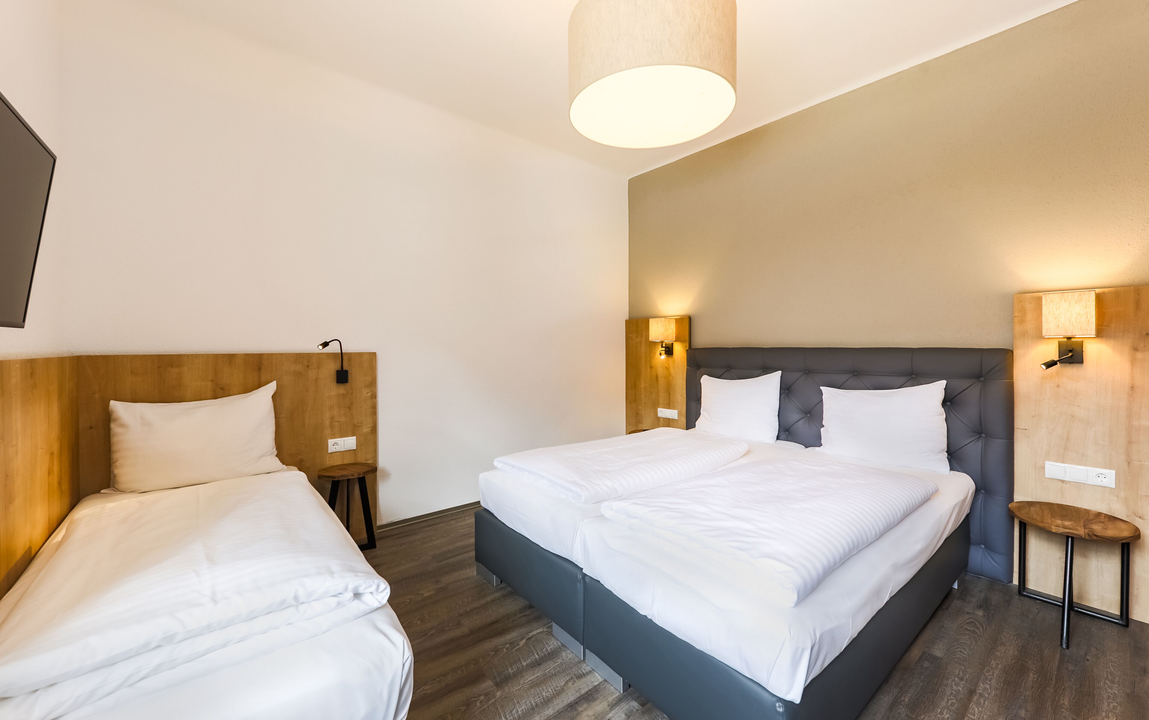 A hotel room with two single beds, wooden headboards, and modern wall sconces.