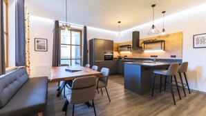 A modern kitchen with a central island, bar stools, and a dining area with a table and chairs. - Kitz Residenz by Alpin Rentals - incl Summercard (Kaprun)