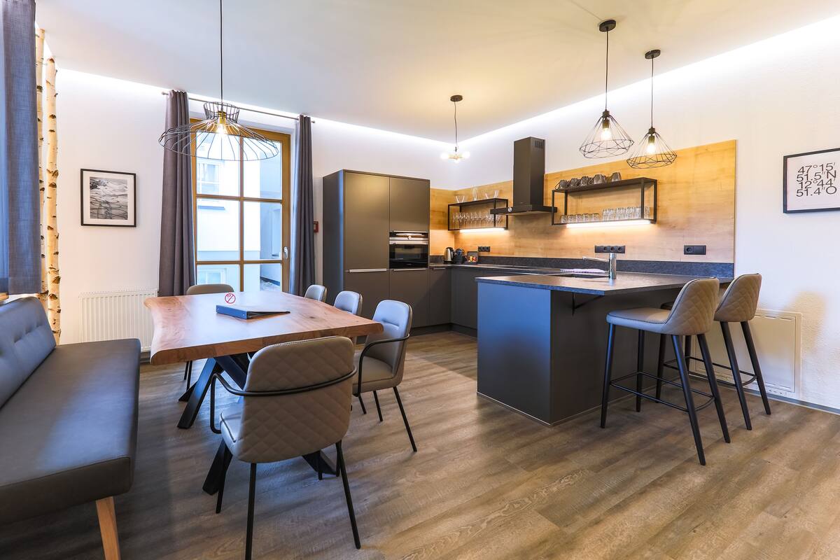 Cozinha moderna com ilha central, banquetas de bar e área de refeições com mesa e cadeiras.