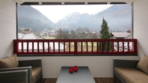 A balcony with wicker furniture and a table, overlooking a mountainous landscape with houses and a red railing. - Kitz Residenz by Alpin Rentals - incl Summercard (Kaprun)