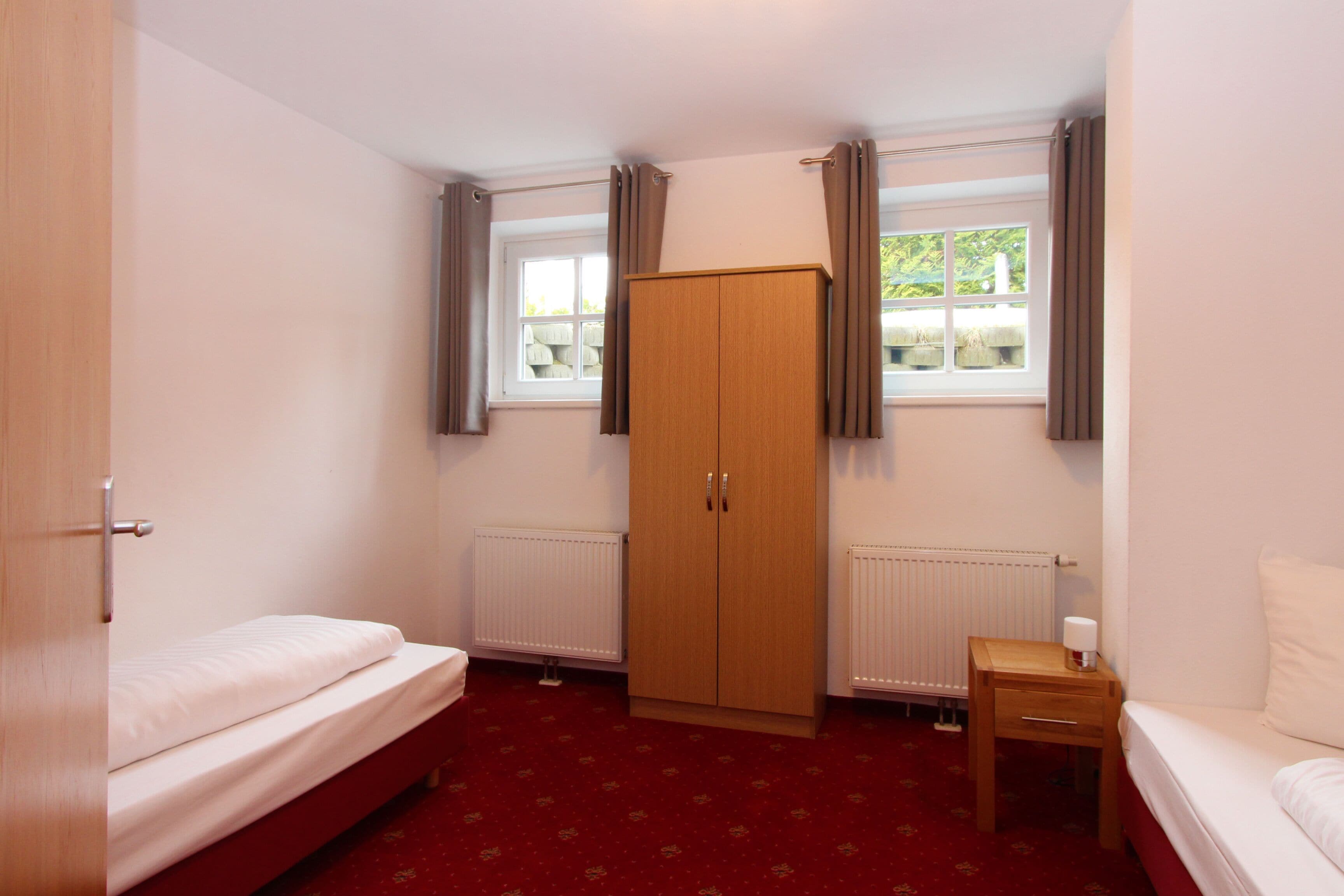 Une chambre à coucher avec un lit simple, une armoire, une table de chevet et une fenêtre avec des rideaux.