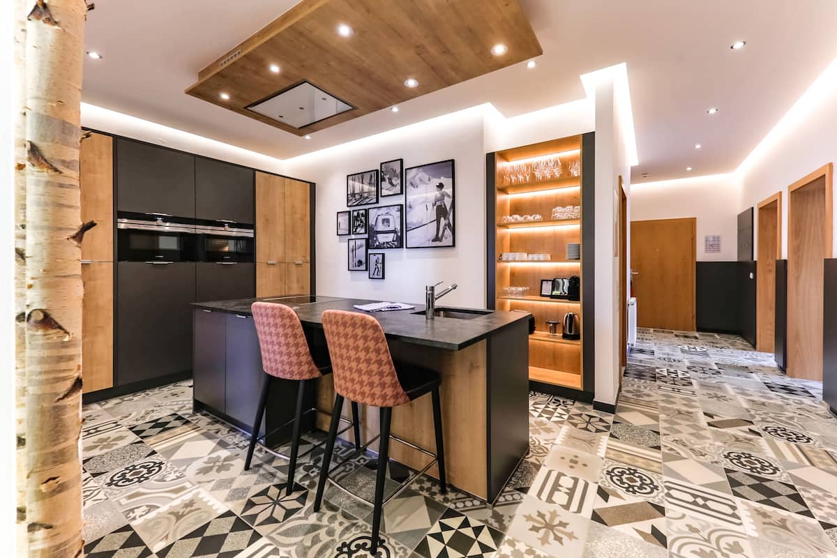 Uma cozinha moderna com ilha central, banquetas de bar e piso estampado.