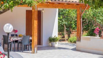 An outdoor patio with a wooden pergola, a table with chairs, and potted plants.