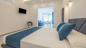A modern hotel room with a large bed, a flat-screen TV mounted on the wall, and a view of the outdoor seating area. - Case Vacanza Loria (San Vito Lo Capo)
