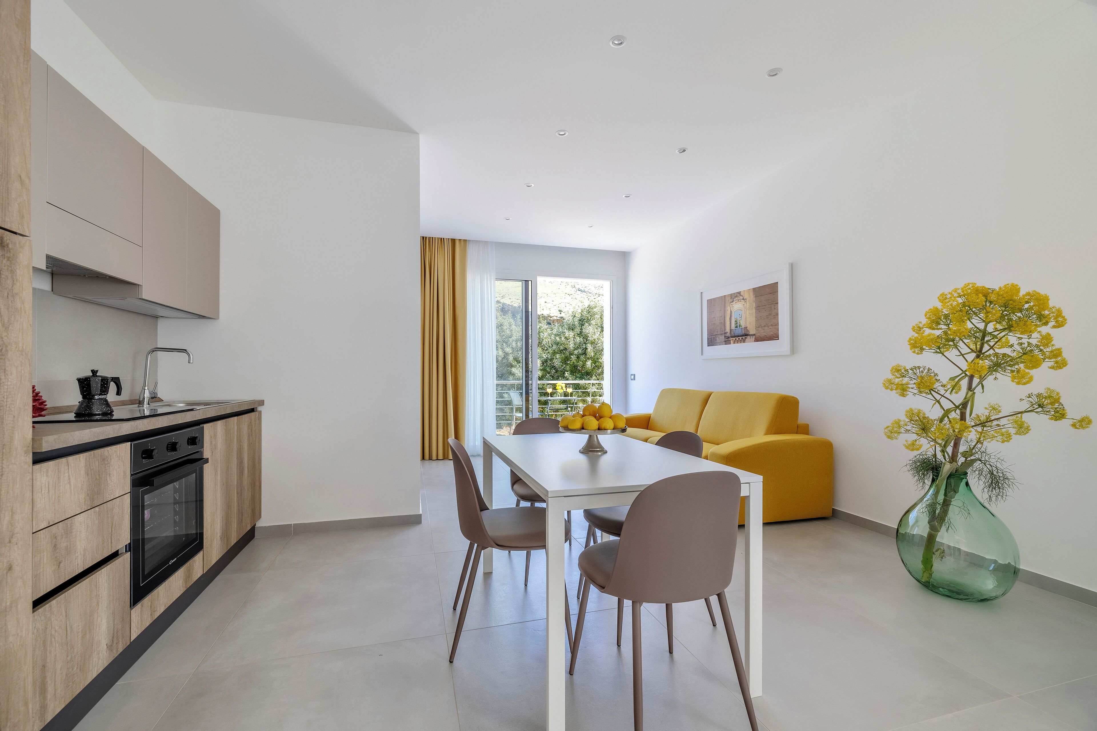 Una cocina moderna con comedor, un sofá amarillo y un amplio ventanal con vistas a zonas verdes.