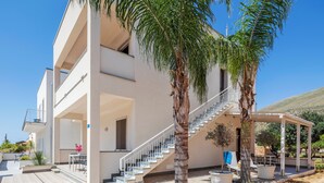 A modern two-story building with a covered outdoor area, a staircase, and palm trees. - Case Vacanza Loria (San Vito Lo Capo)