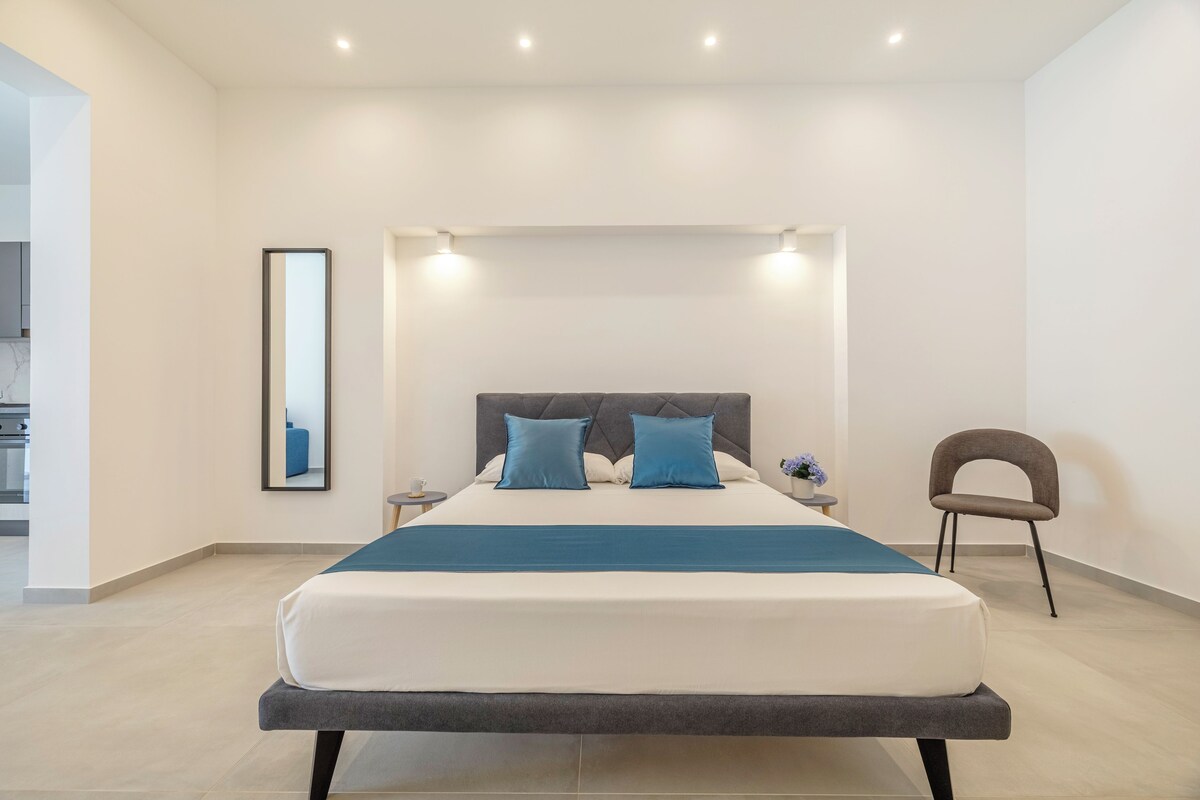 Un dormitorio moderno con una cama grande, una mesita de noche, una silla y un espejo en la pared.
