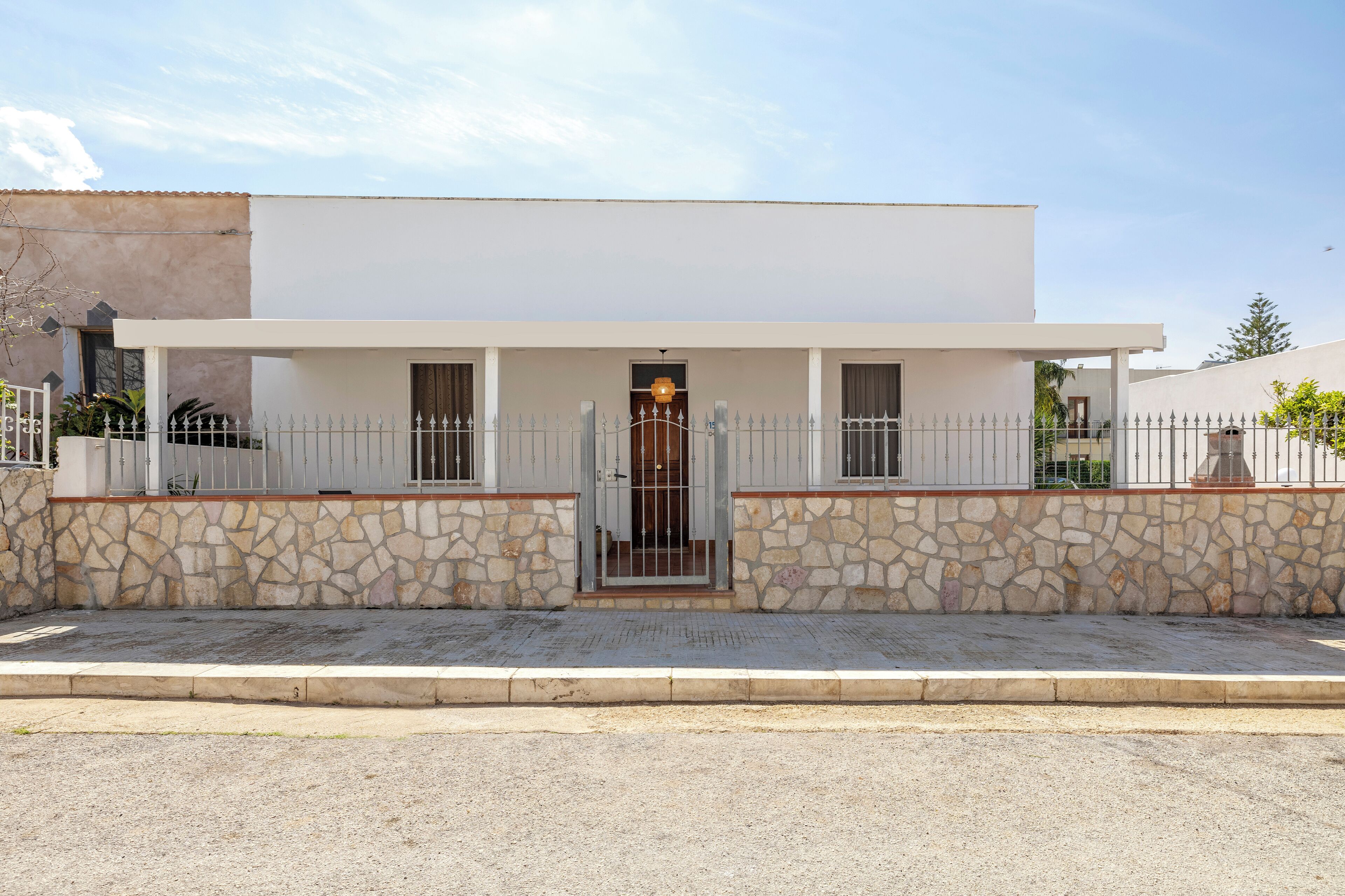 A modern two-story house with a stone facade, a gated entrance, and a small porch.