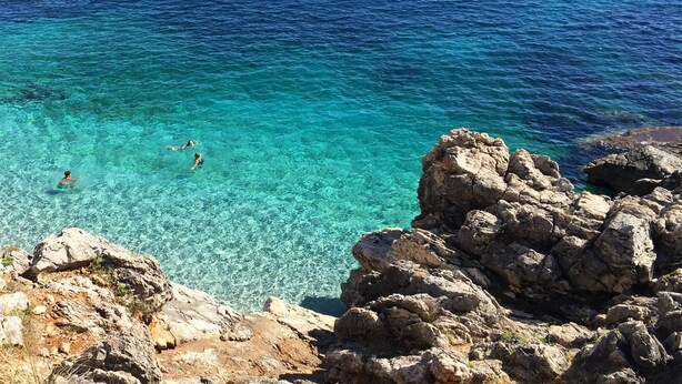 A rocky coastline with clear turquoise water and people swimming. - Case Vacanza Loria (San Vito Lo Capo)
