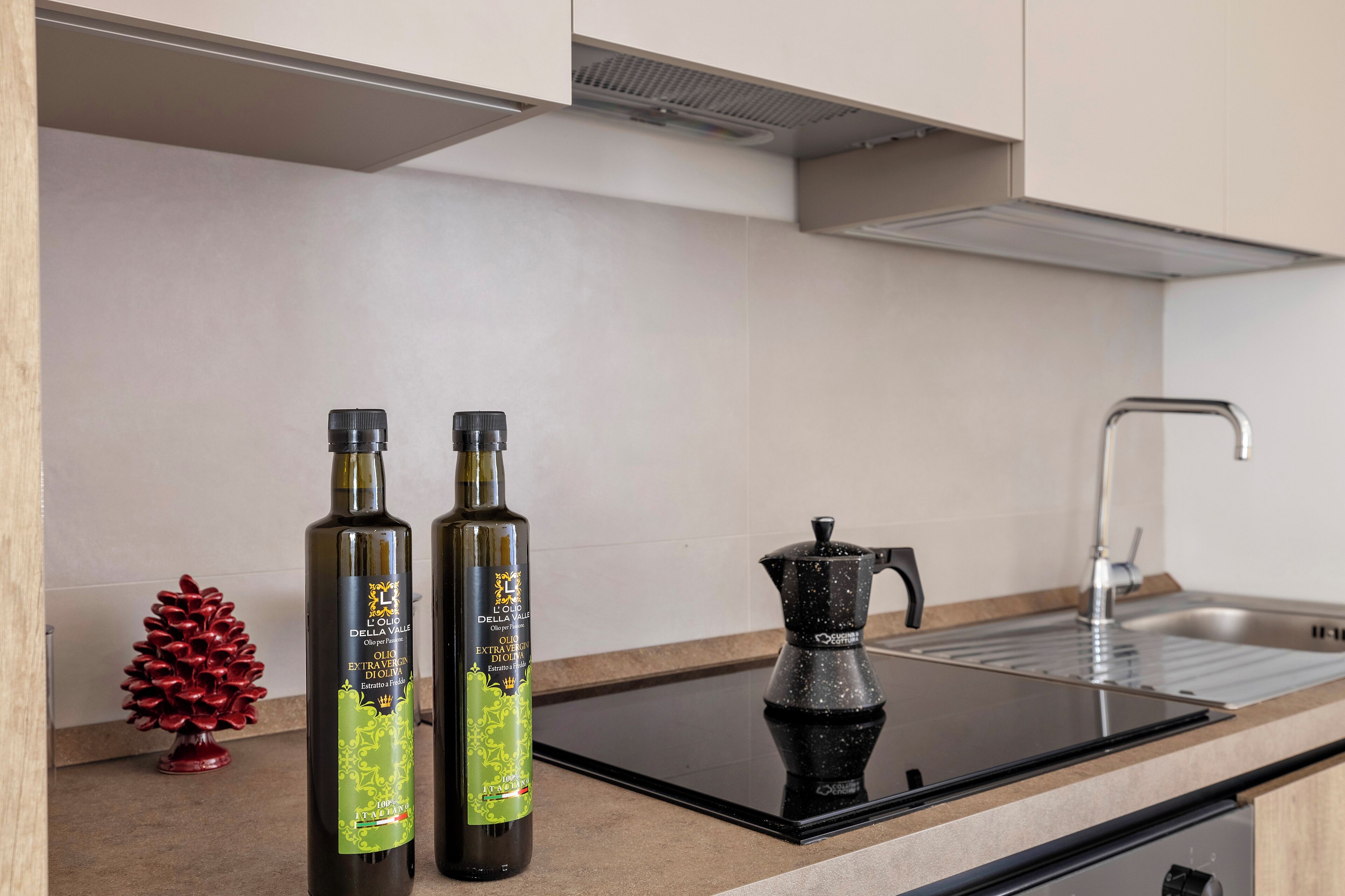 A kitchen with two bottles of olive oil, a coffee maker, and a small decorative pine cone.
