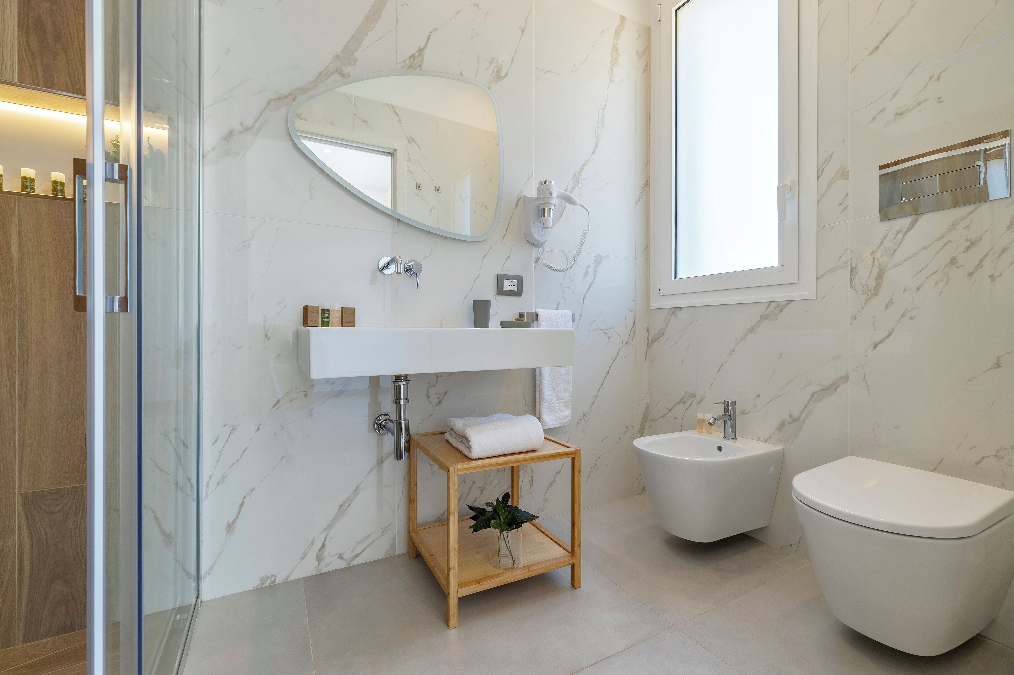 Un baño moderno con pared de mármol, tocador de madera, un bidé y un inodoro.
