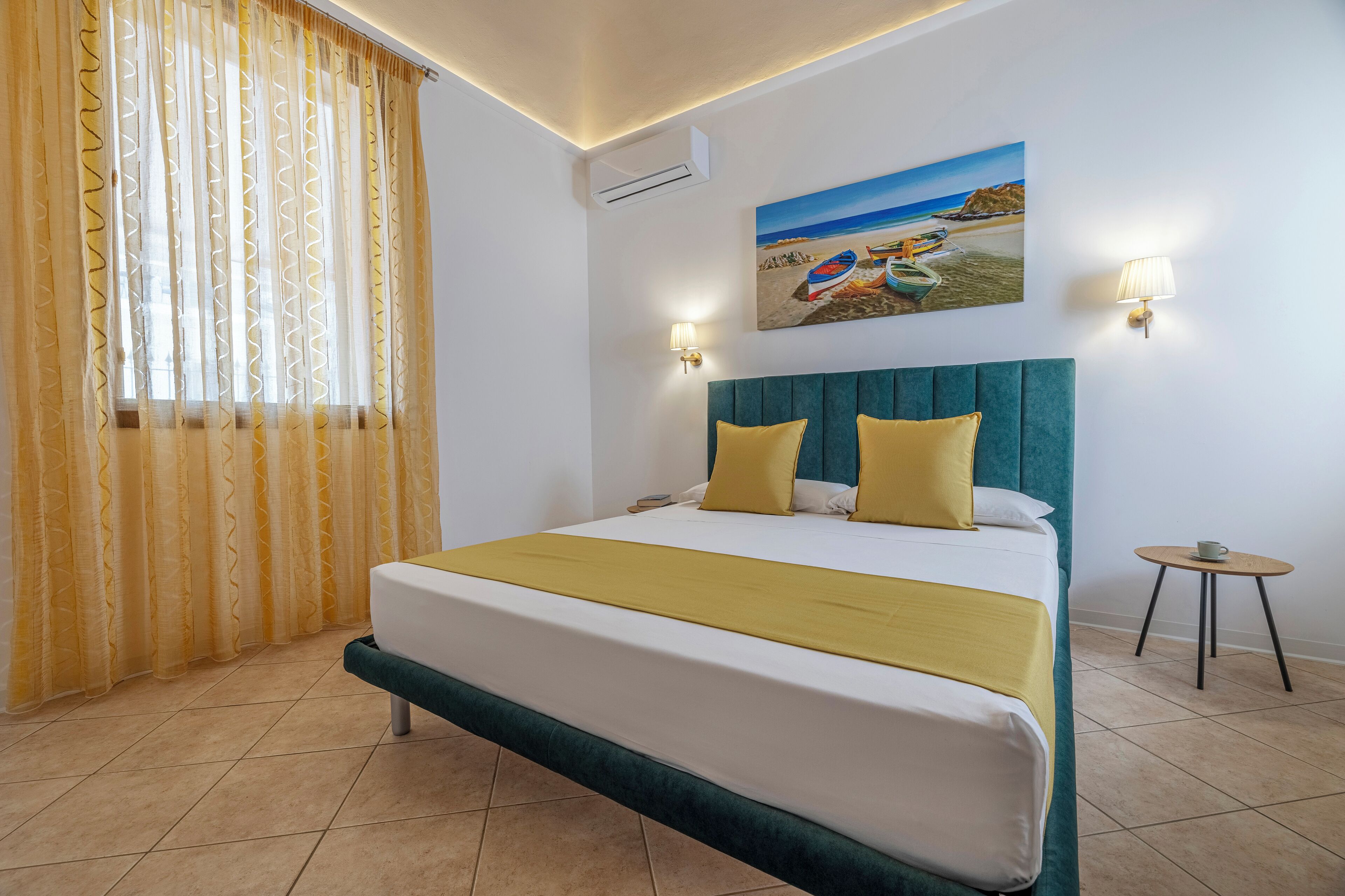 Een hotelkamer met een bed, een schilderij van boten op een strand en twee wandlampen.