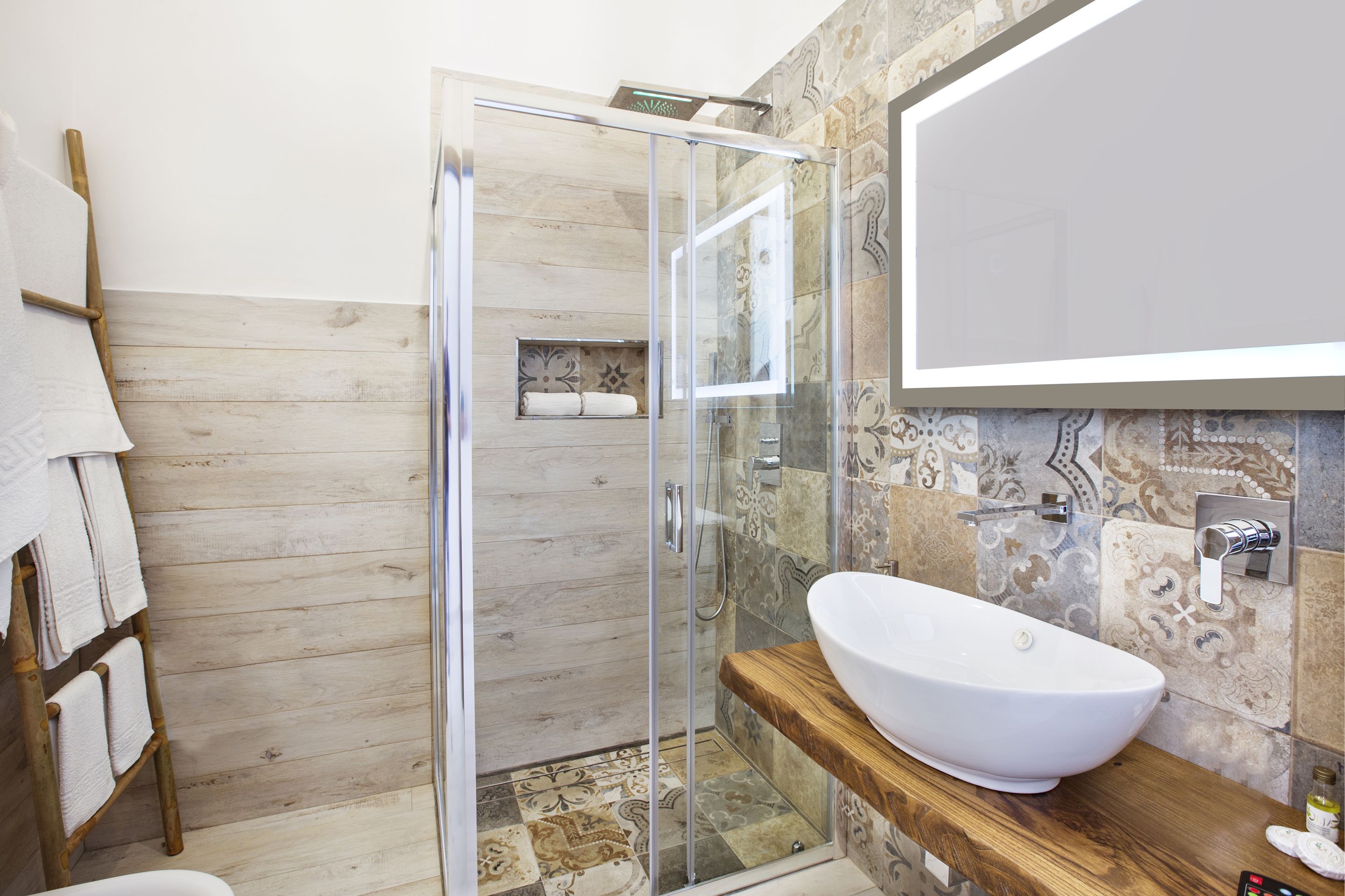 Ein modernes Badezimmer mit Duschkabine aus Glas, einem Holzkosmetikschrank mit großem Aufsatzbecken und einer gefliesten Rückwand.