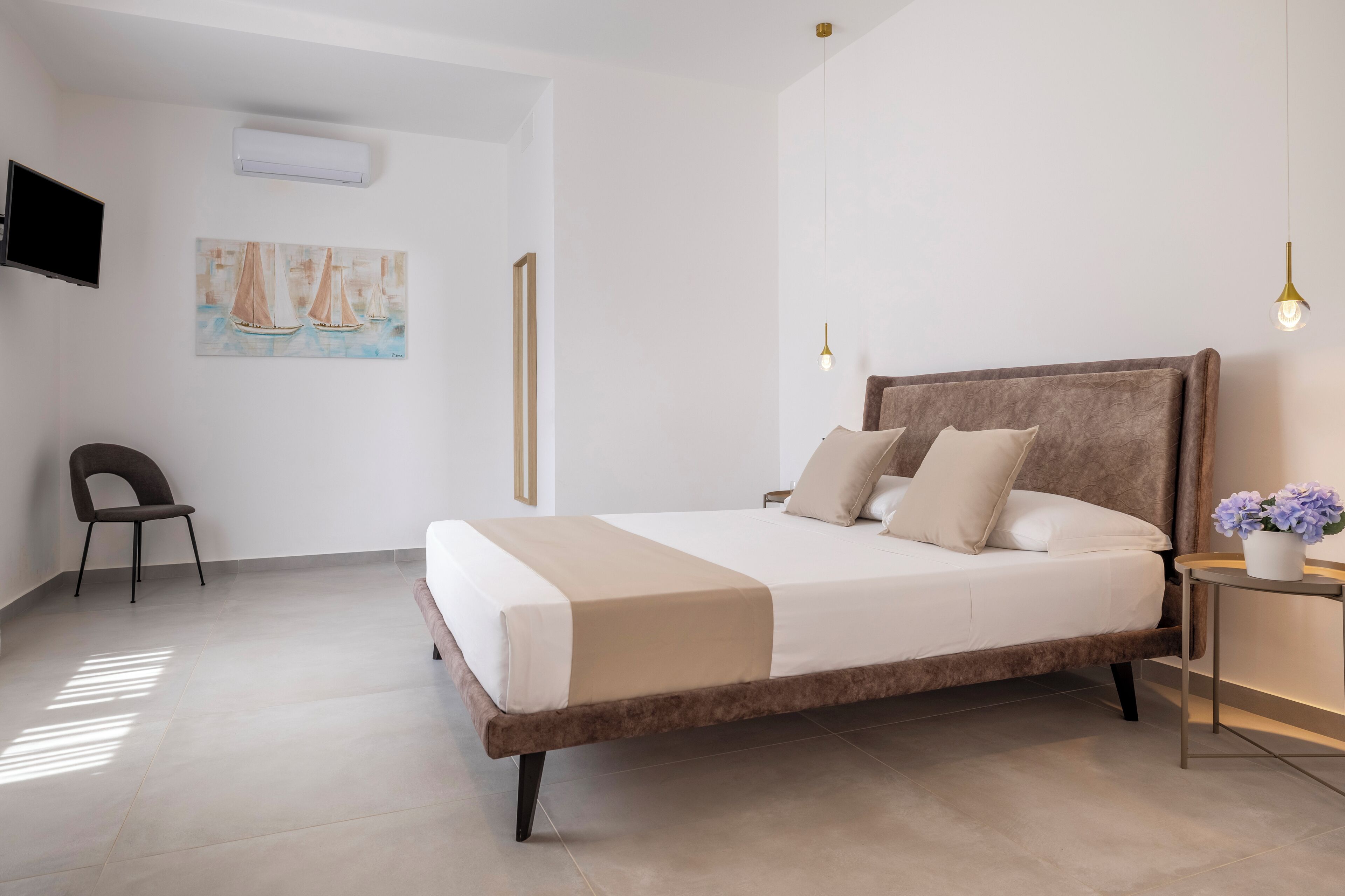 Quarto moderno com cama grande, uma poltrona, televisão e um quadro na parede.