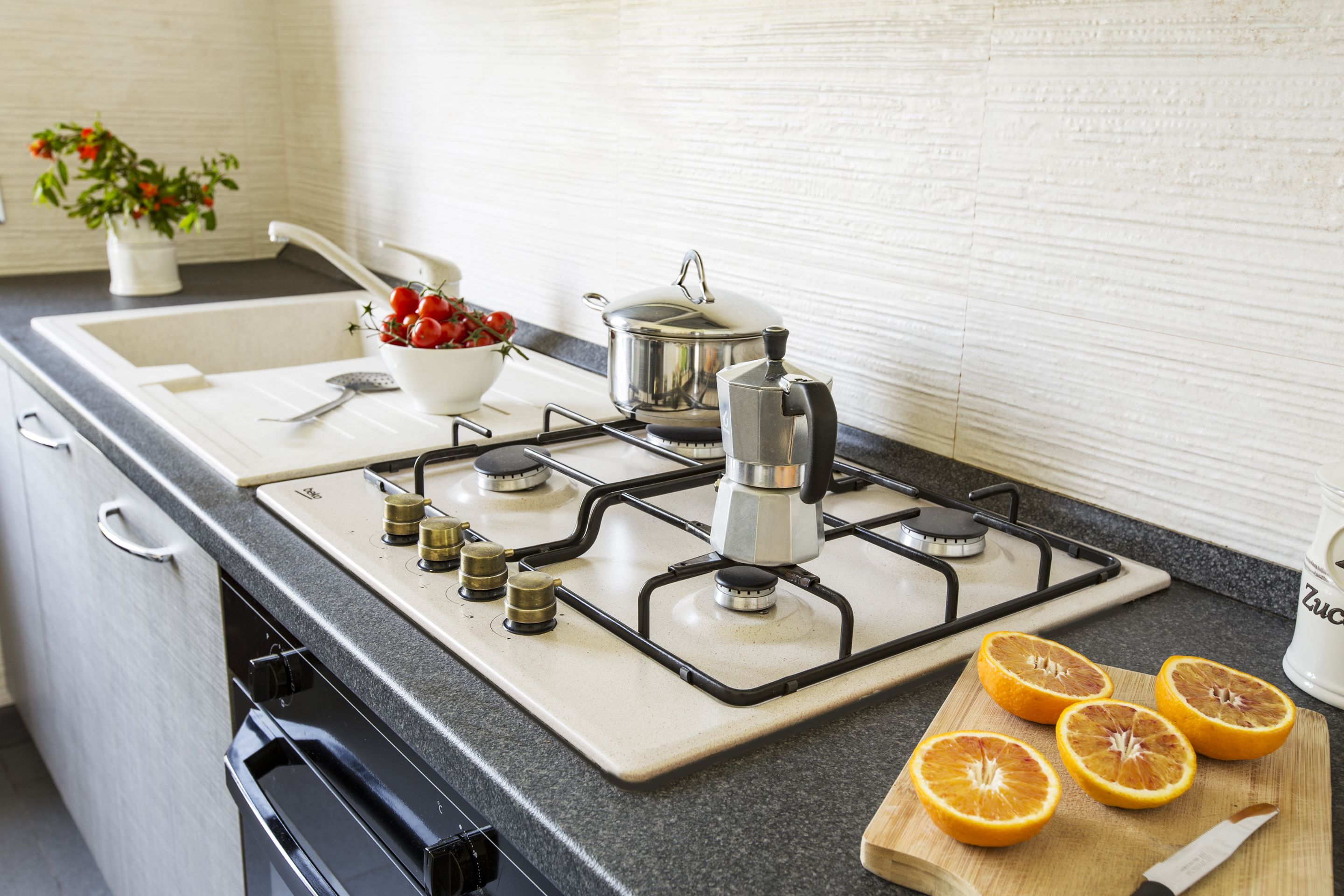 Una cocina con estufa a gas, un lavamanos y una tabla de cortar con rodajas de naranja.