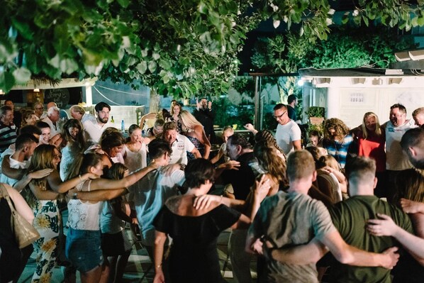 Un evento al aire libre concurrido, con gente bailando y socializando bajo un árbol.