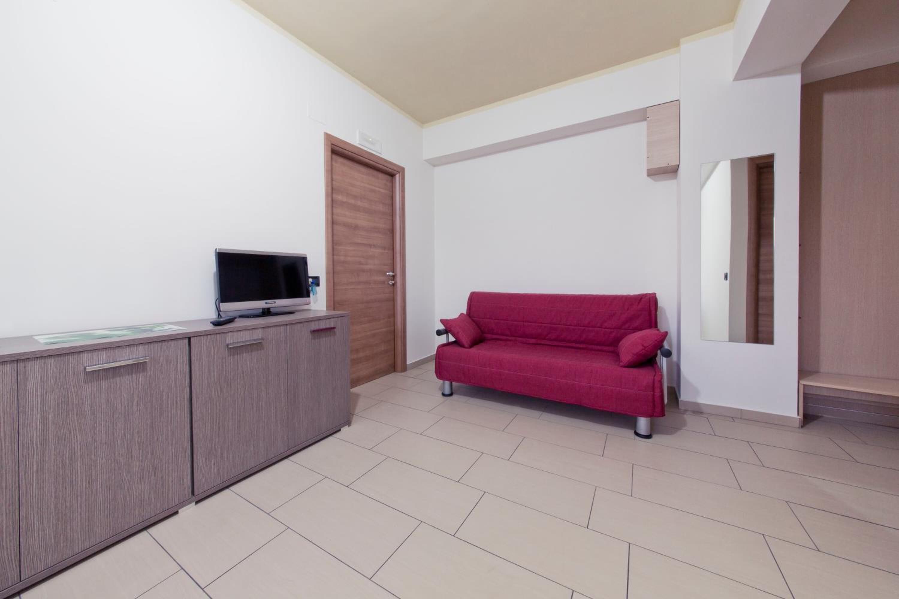 Una habitación con un armario de madera, un sofá rojo, un televisor y una puerta.
