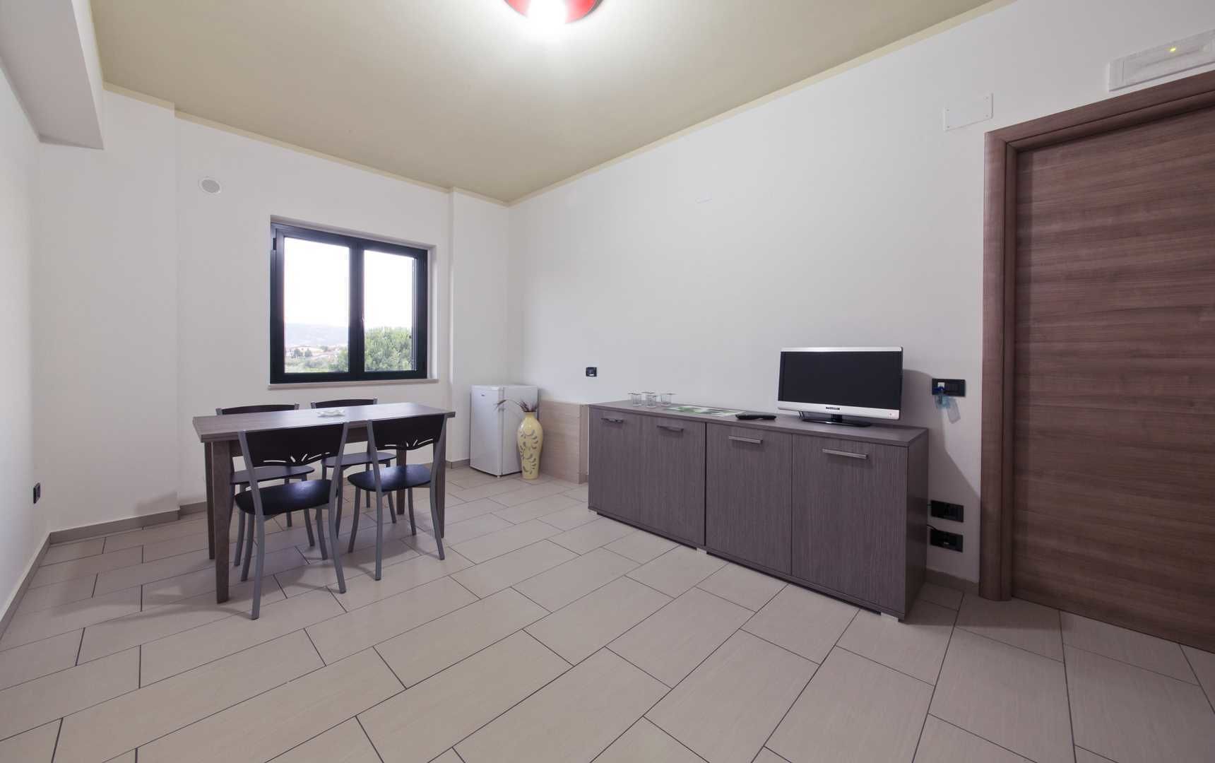 A modern kitchen with a dining area, a large window, and a TV.
