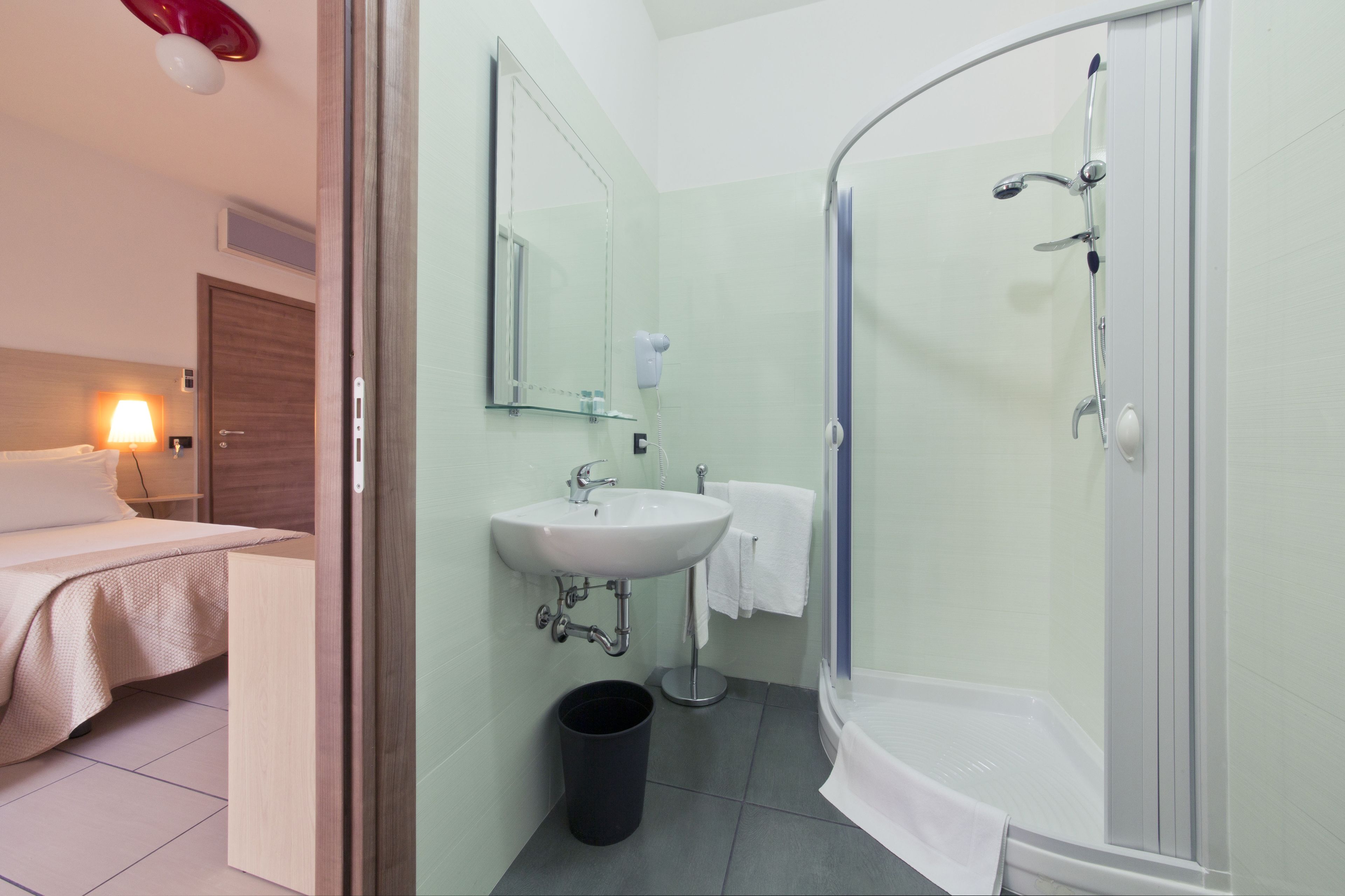 A bathroom with a sink, mirror, shower, and a trash bin.