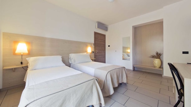 Quarto de hotel com duas camas, uma escrivaninha e uma cadeira.