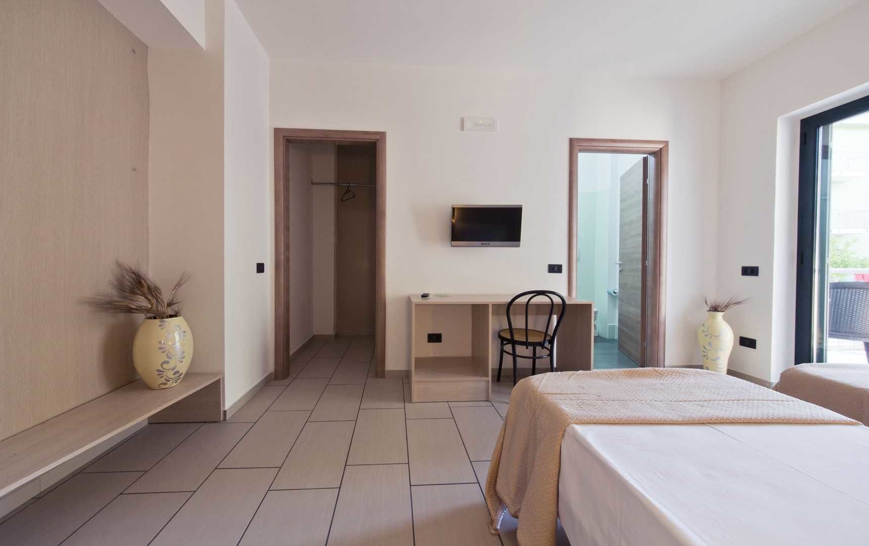 Una habitación de hotel con cama, escritorio, silla, televisor y un ventanal grande.
