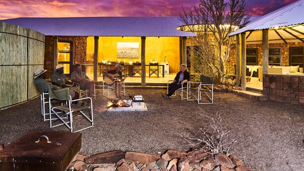 Een terras met stenen muren en een vuurkorf, omringd door metalen stoelen en tafels.