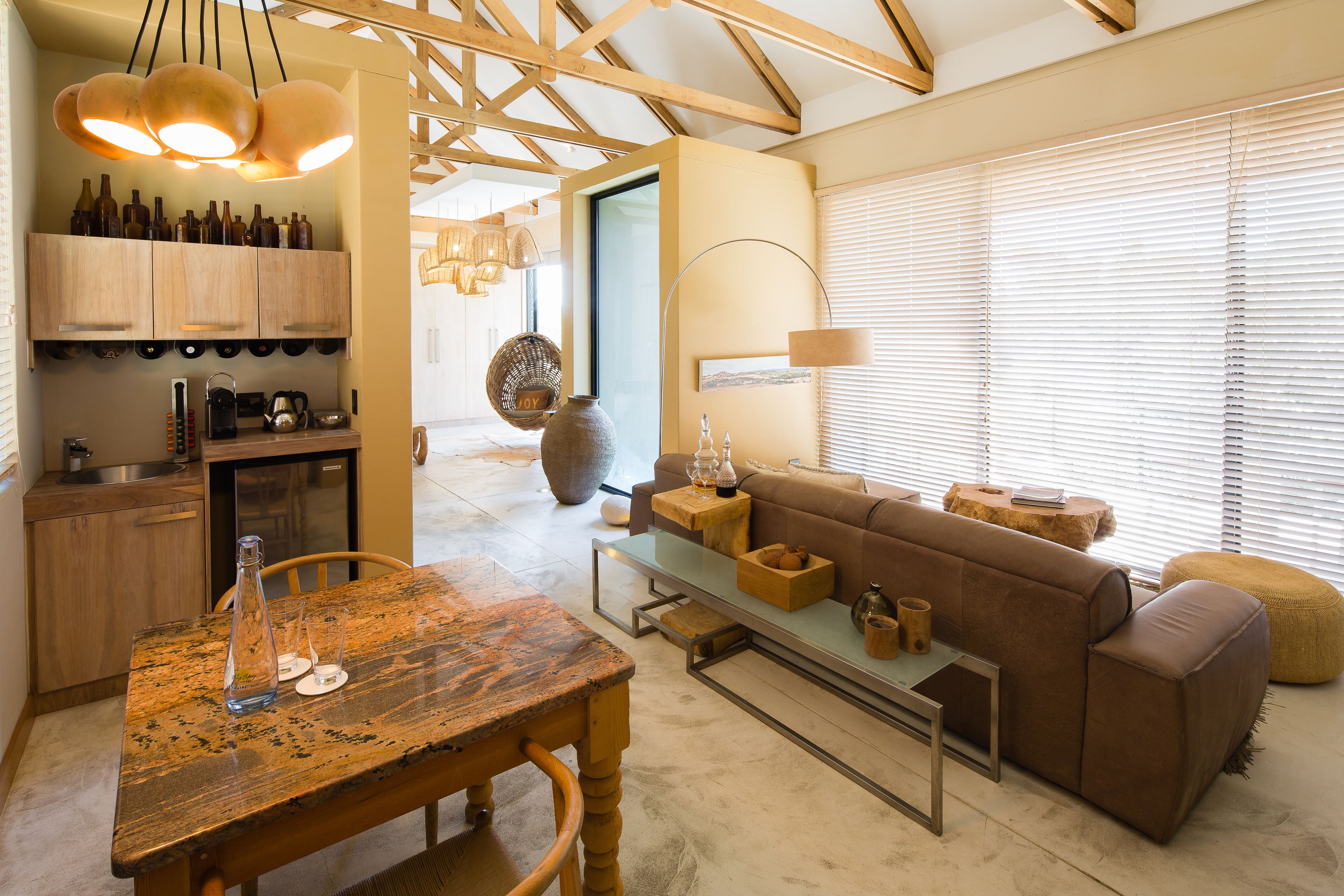 A modern kitchen with wooden cabinets, a dining table, and a cozy living area with a sofa and ottoman.