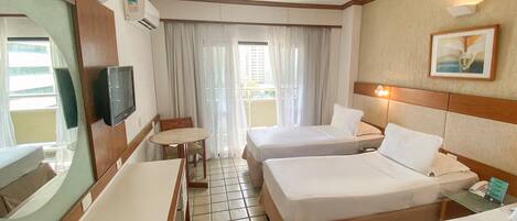 Habitación de hotel con dos camas, un escritorio, una silla, un televisor, una ventana con cortinas y un cuadro en la pared.