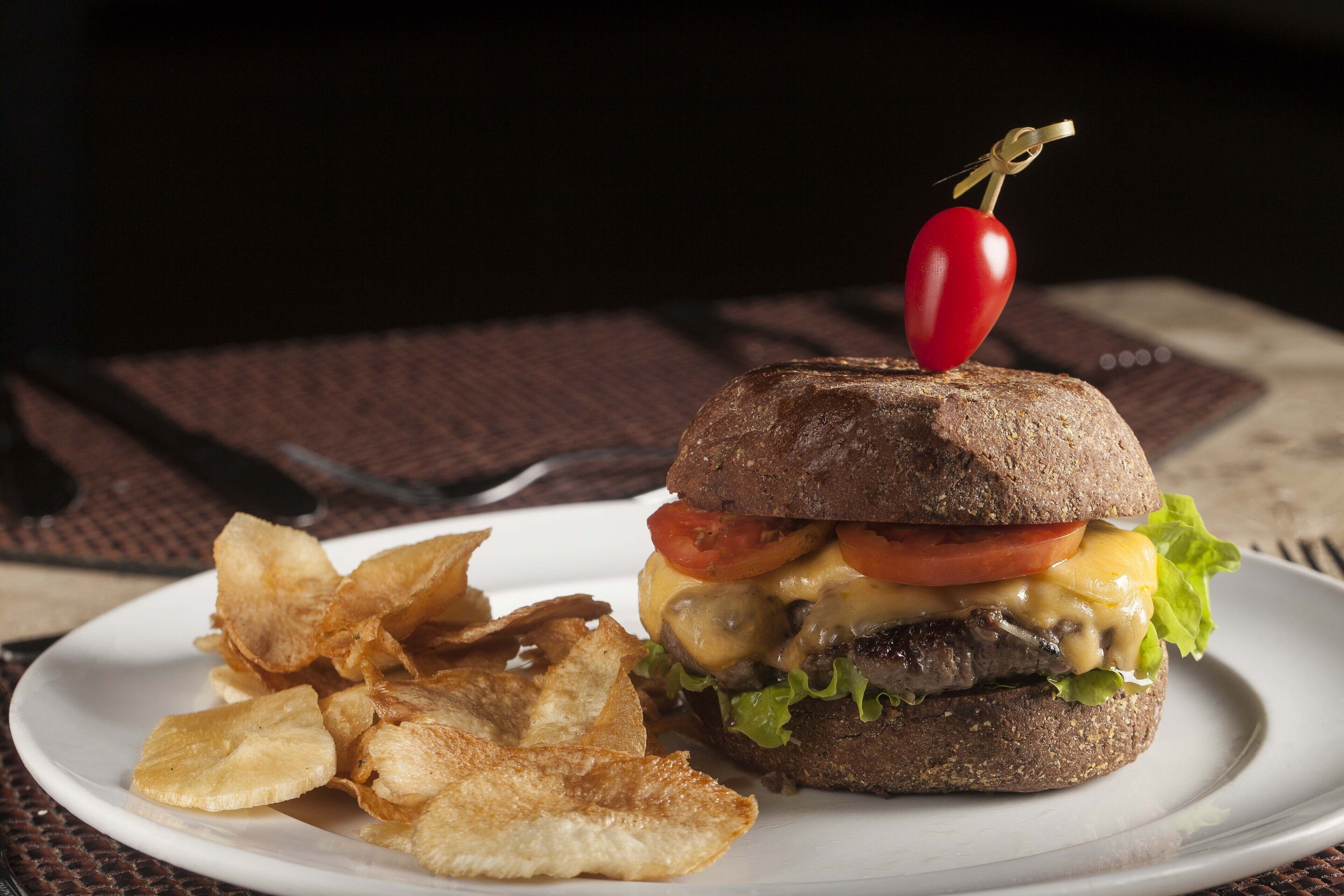 Un sandwich garni d’un piment rouge, servi avec des chips sur une assiette blanche.