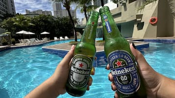 Piscina com espreguiçadeiras e palmeiras, cercada por edifícios altos.