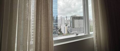 Una ventana con cortinas, vista de un paisaje urbano con edificios y cielo despejado.