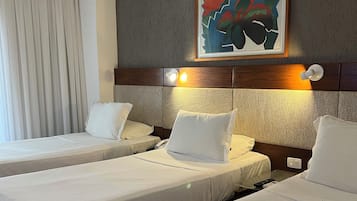 A hotel room with two beds, a painting on the wall, and a window with curtains.