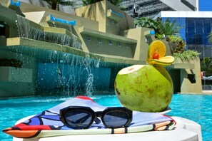 A pool area with a water feature and a surfboard with sunglasses and a fruit. - Mar Hotel Conventions (Recife)