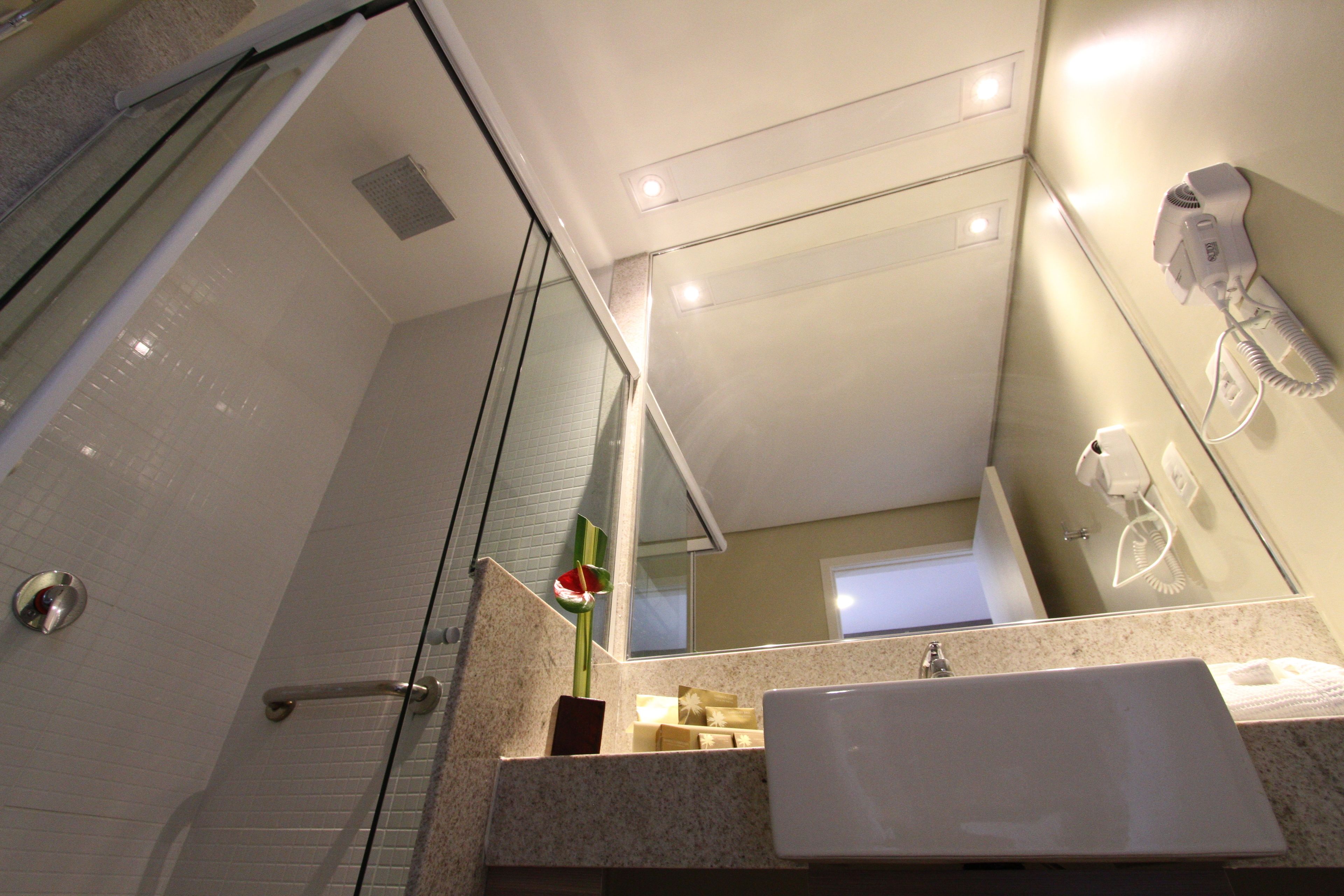 Un baño moderno con cabina de ducha de vidrio, un lavamanos con toalla y un secador de pelo montado en la pared.