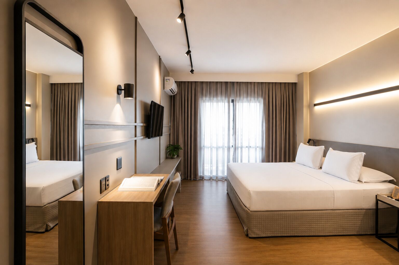 Habitación de hotel con cama, escritorio, silla, televisor y un espejo grande.