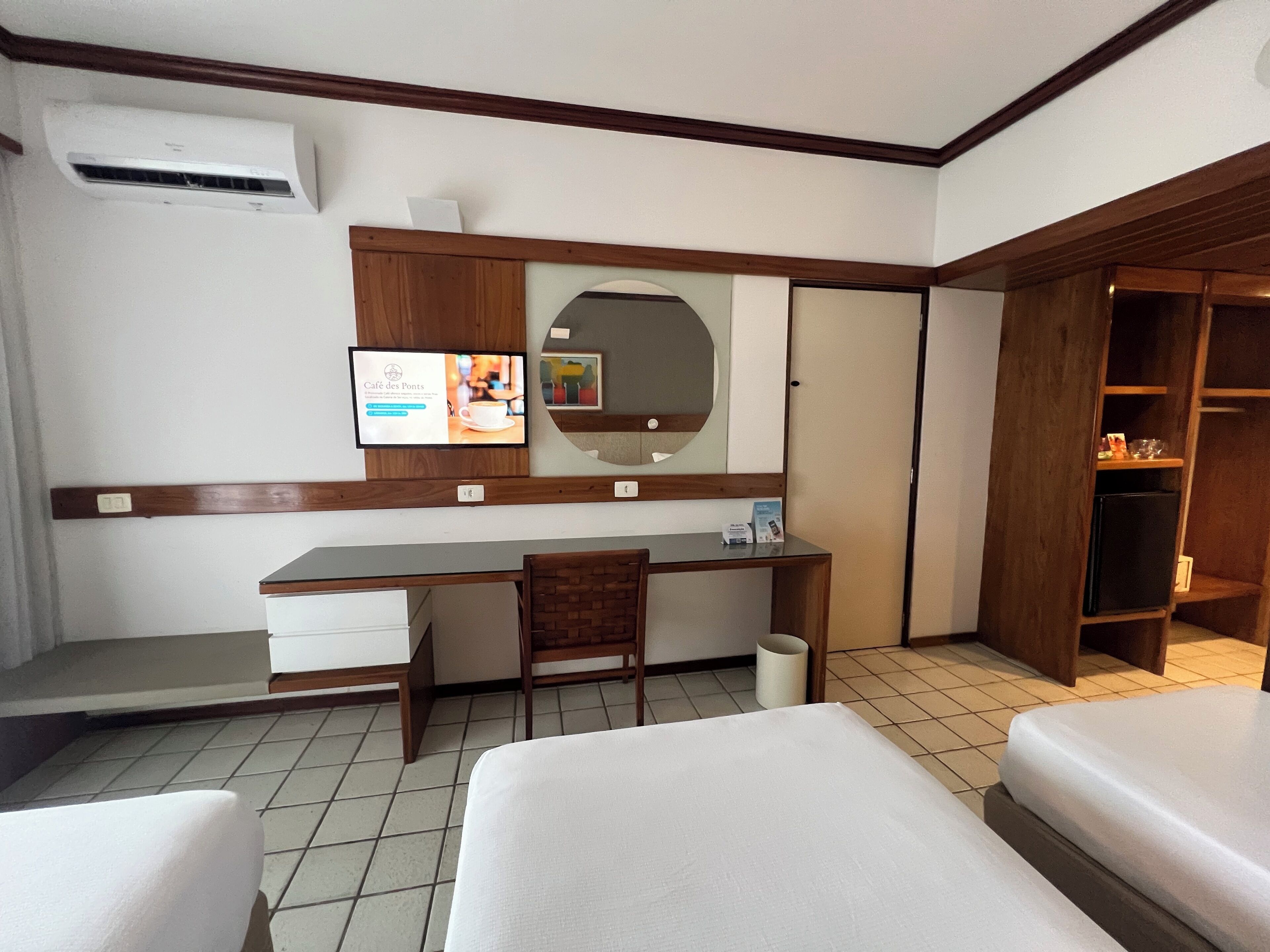 Una habitación de hotel con escritorio, silla, dos camas, espejo y armario.
