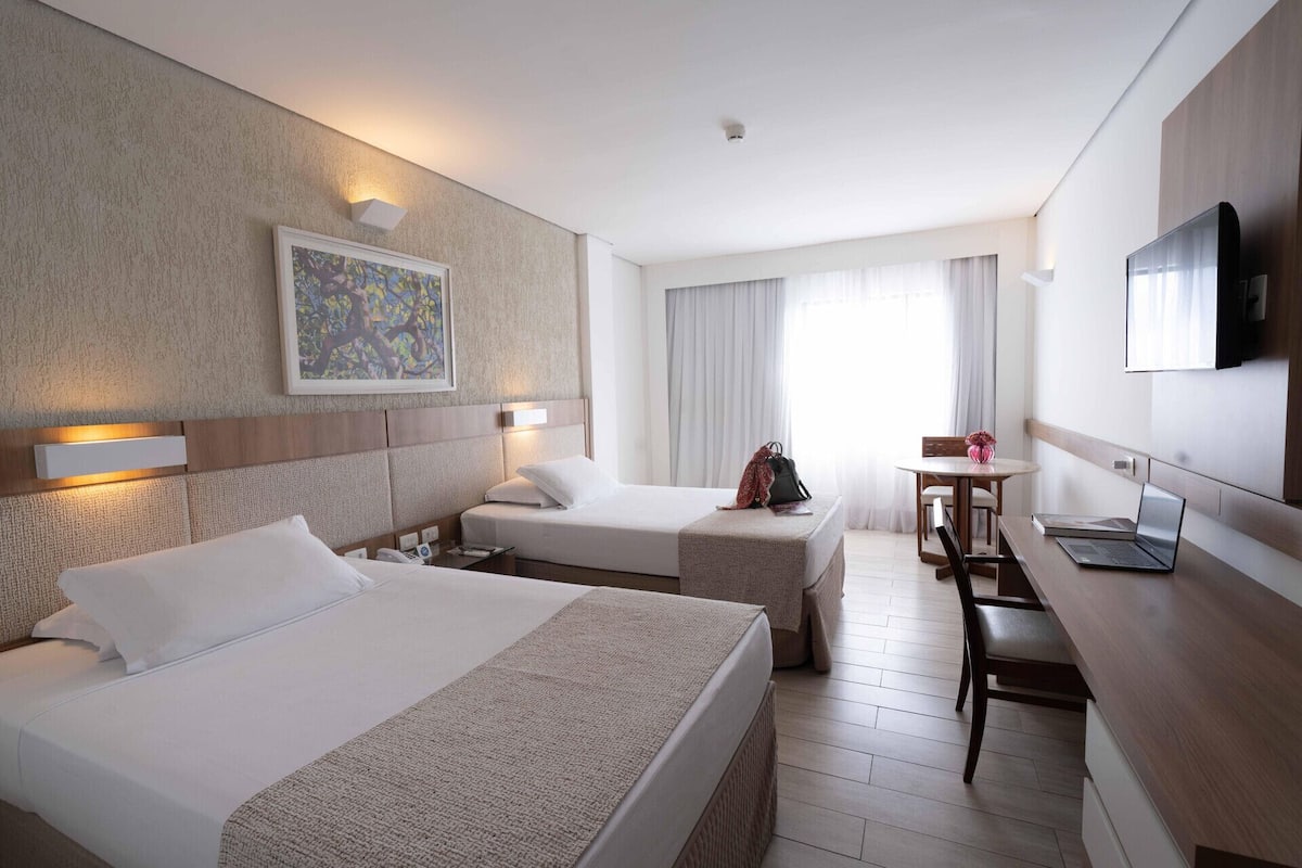Une chambre d’hôtel avec deux lits, un bureau, une chaise, une télévision et un tableau au mur.