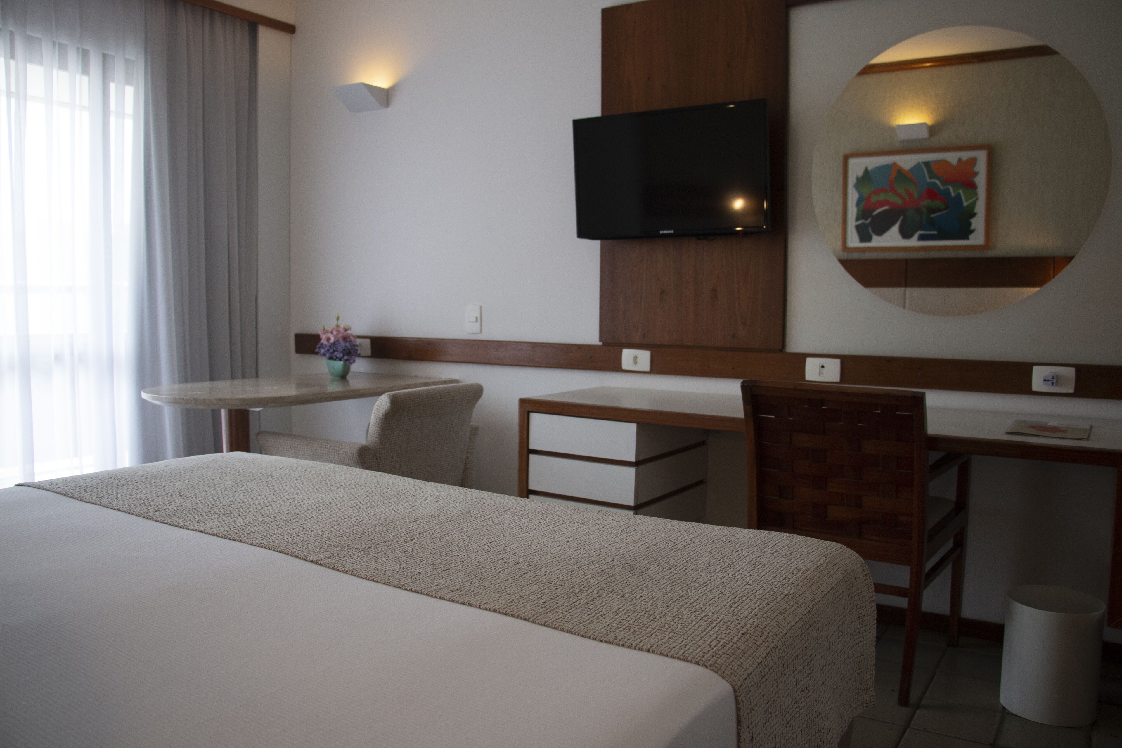 A hotel room with a large bed, a desk, a chair, a television, and a wall-mounted artwork.