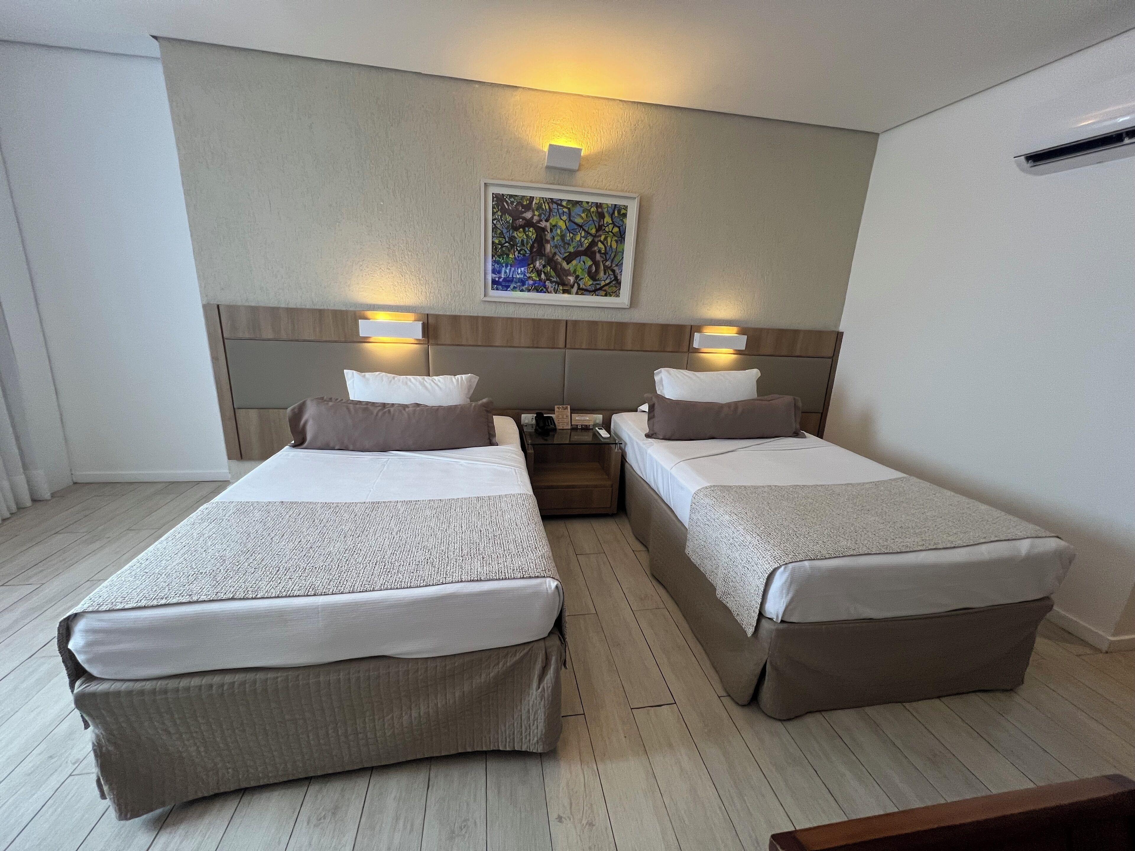 Habitación de hotel con dos camas, cabecero de madera, un cuadro enmarcado en la pared y una mesita con un teléfono.