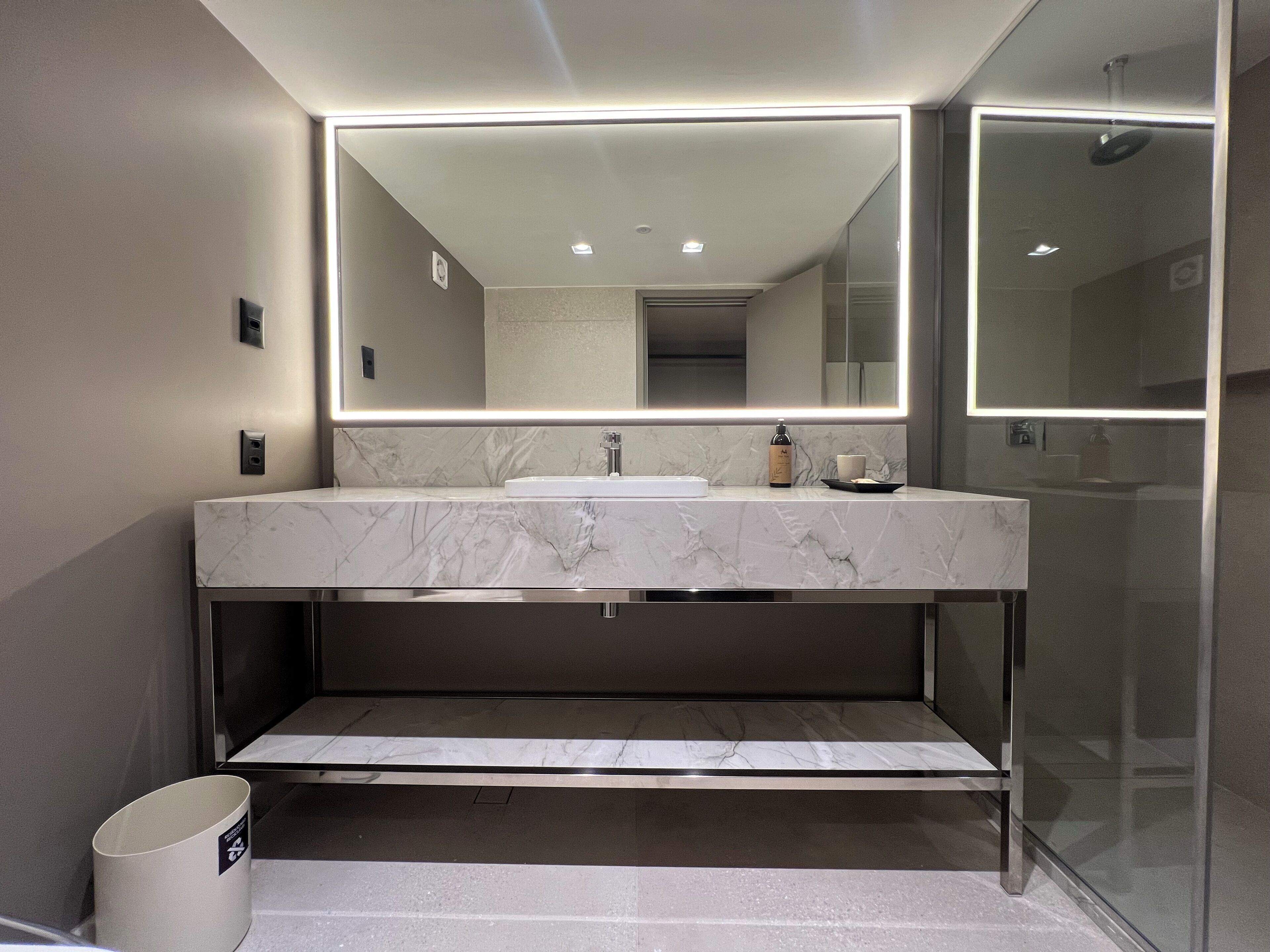 A modern bathroom with a marble sink, a large mirror, and a glass shower enclosure.