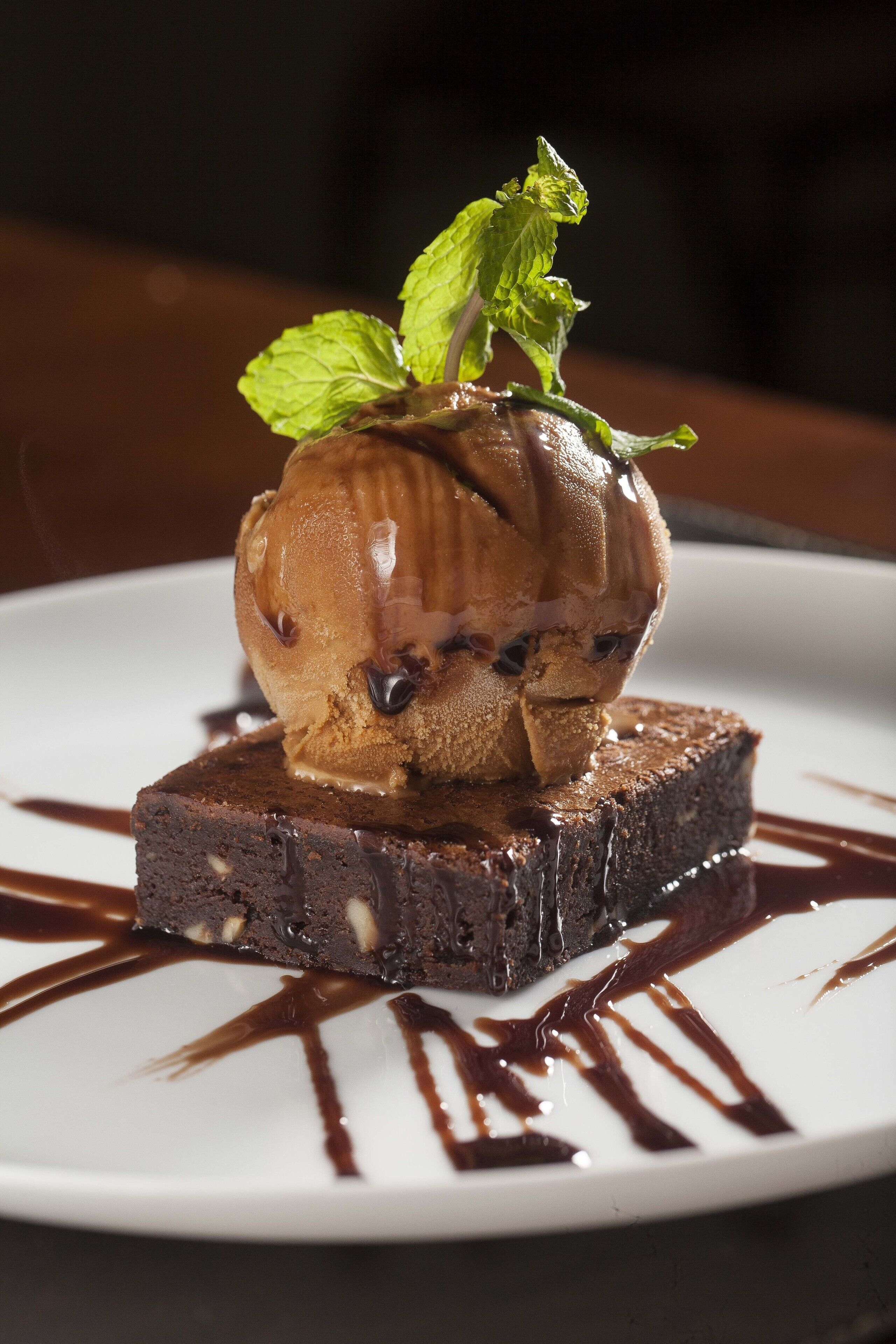 Un dessert composé d’une boule de glace au chocolat posée sur un brownie, le tout garni de feuilles de menthe.