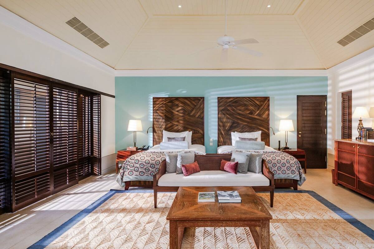 A hotel room with two beds, a wooden coffee table, a desk with a lamp, and a wardrobe.