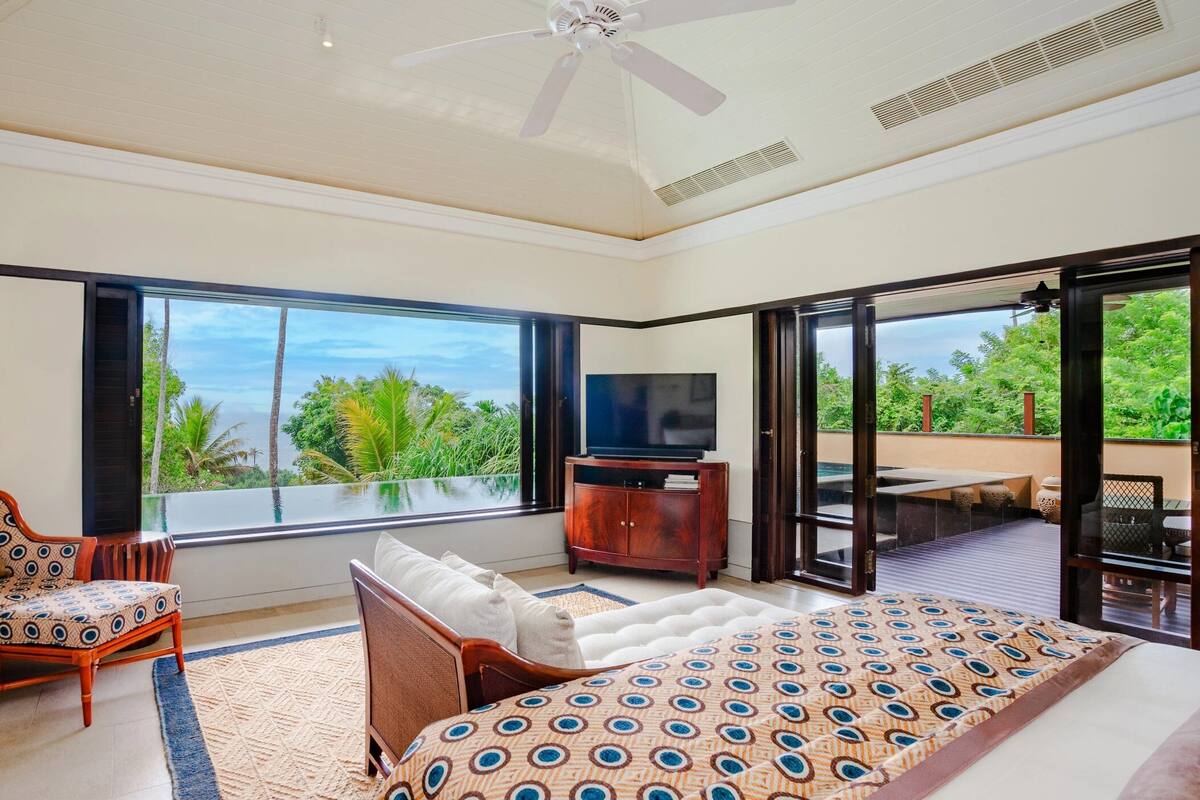 A spacious bedroom with a large bed, a TV, a chair, and a view of the outdoors.