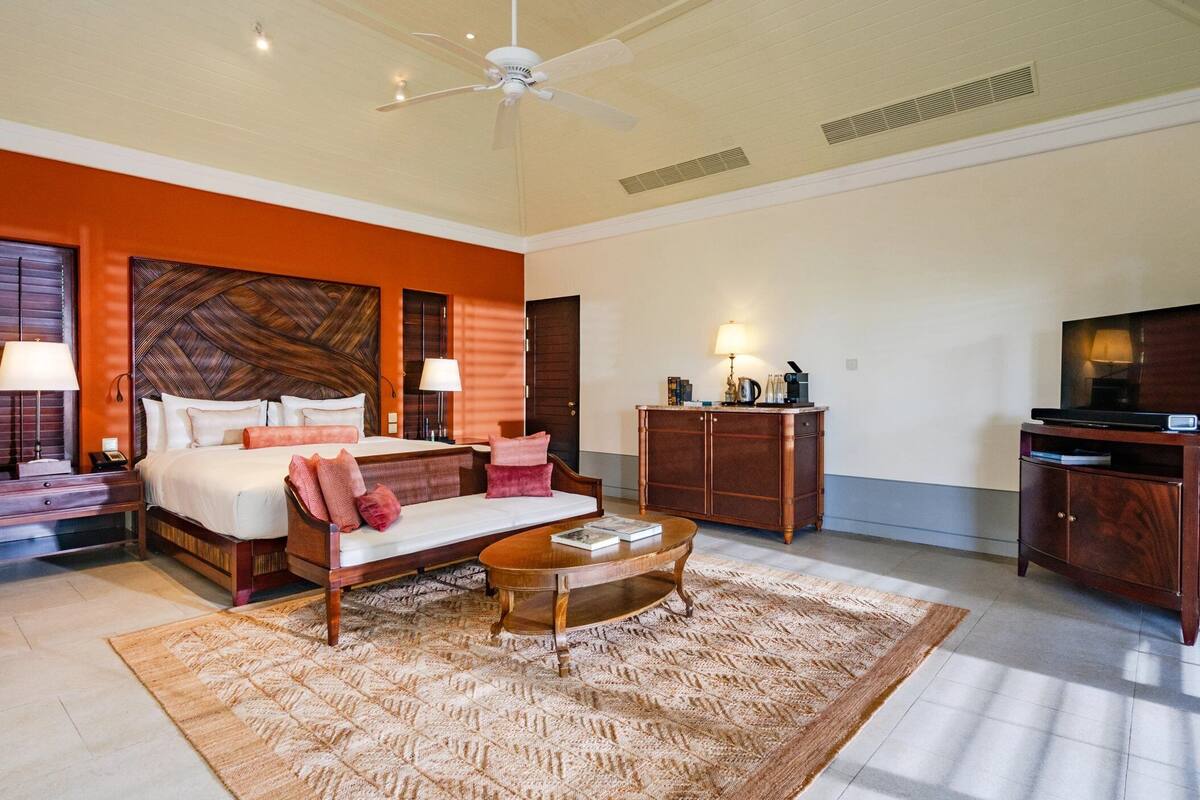A spacious hotel room with a large bed, a sitting area, a television, and a desk with a lamp.