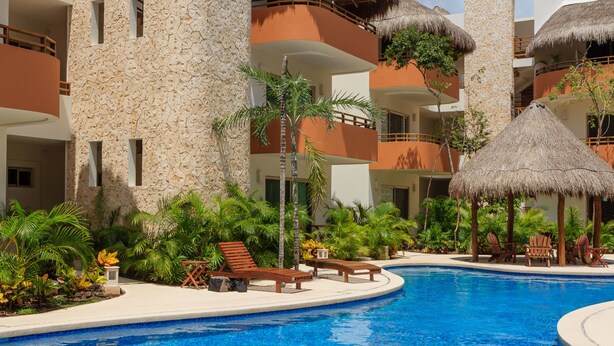 Un resort con piscina, sillas de descanso y sombrillas de paja.